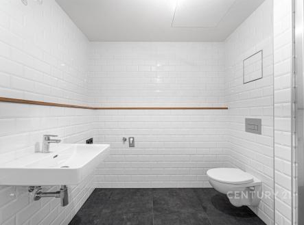 Moderní koupelna s bílými obklady, závěsnou toaletou a umyvadlem. Kombinace dlažby na podlaze a čistý design vytváří světlý prostor. | Prodej bytu, 1+kk, 45 m²