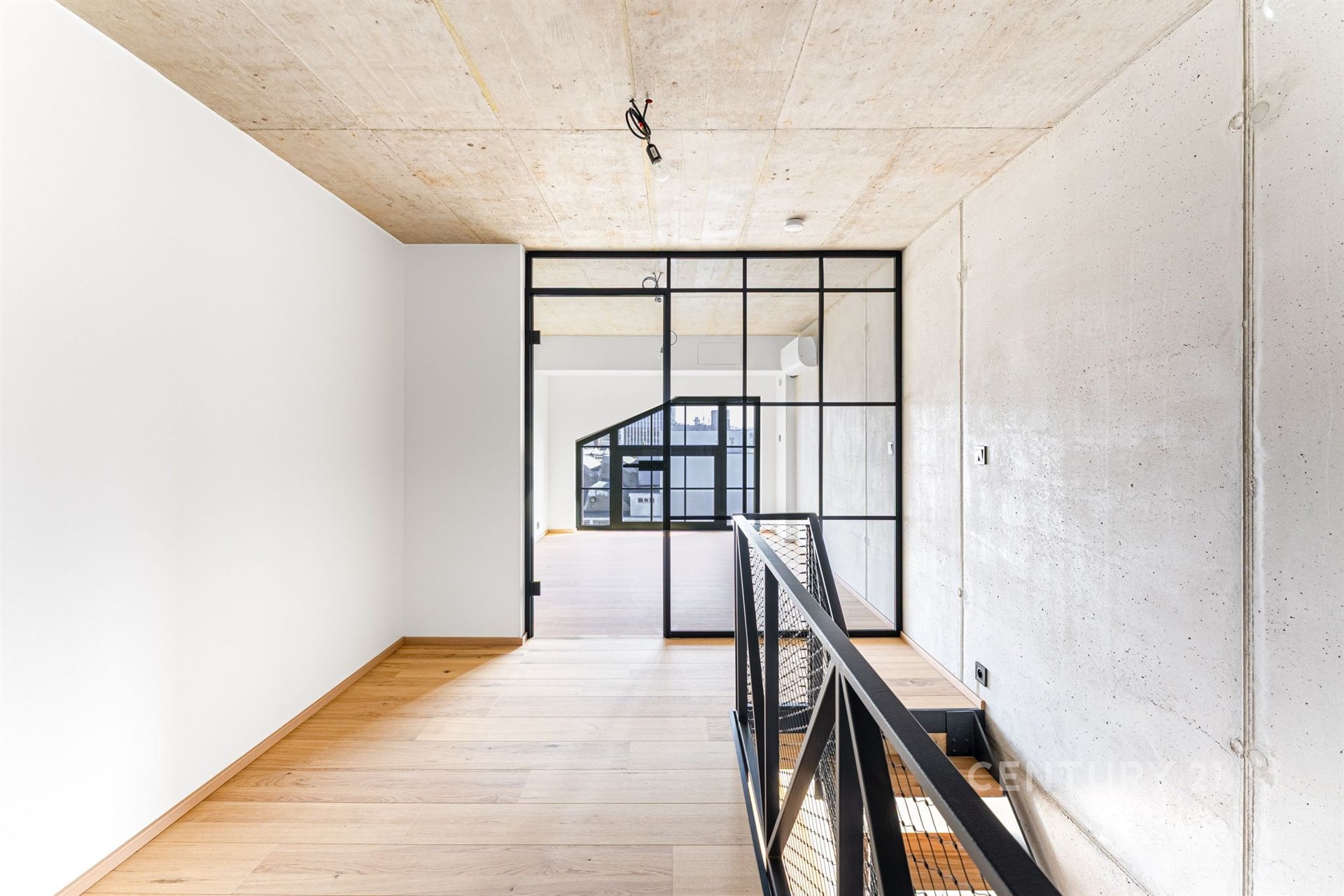 Průmyslová chodba s parketovou podlahou, industriálním zábradlím a velkými okny, moderní design s betonovými stropy.