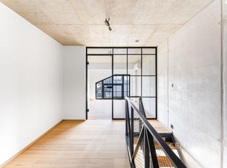 Průmyslová chodba s parketovou podlahou, industriálním zábradlím a velkými okny, moderní design s betonovými stropy. | Prodej bytu, 3+kk, 66 m²