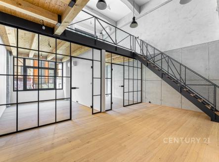 Prostorný moderní obývací pokoj s parketovou podlahou, velkými prosklenými stěnami a kovovým schodištěm, ideální pro loftový styl. | Prodej bytu, 4+kk, 128 m²