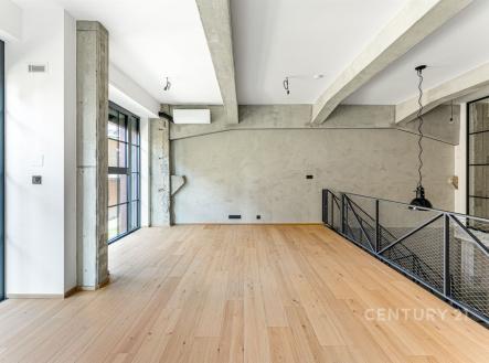 Moderní obývací pokoj s parketovou podlahou, velkými okny a industriálním stylem. Světlý prostor s betonovými trámy a minimalistickým designem. | Prodej bytu, 4+kk, 128 m²