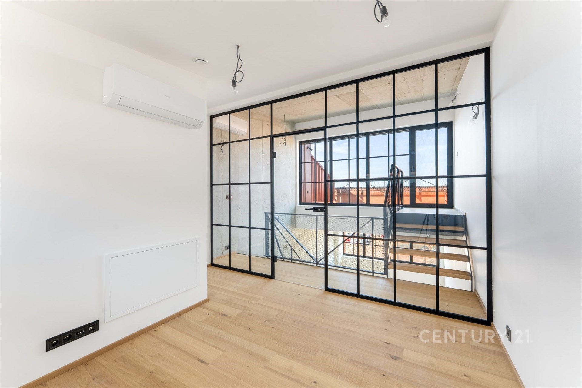 Světlý obývací pokoj s parketovou podlahou a velkými skleněnými dveřmi, moderní design a klimatizace zvýrazňují jeho stylovou úpravu.