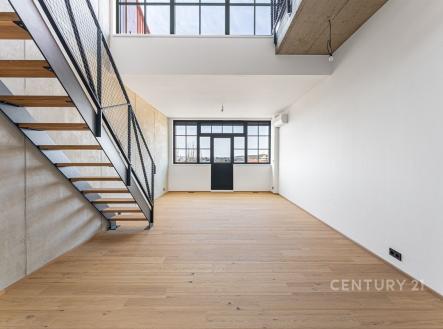 Světlý obývací pokoj s parketovou podlahou a velkými okny, moderní design s kovovým schodištěm a betonovým stropem. | Prodej bytu, 2+kk, 65 m²