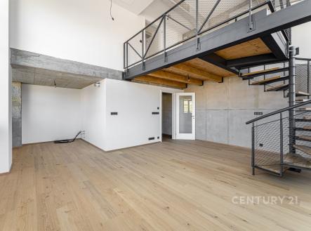 Loftový obývací prostor s dřevěnou podlahou, moderní betonové stěny, kovové schodiště a velká okna poskytující dostatek světla. | Prodej bytu, 4+kk, 110 m²