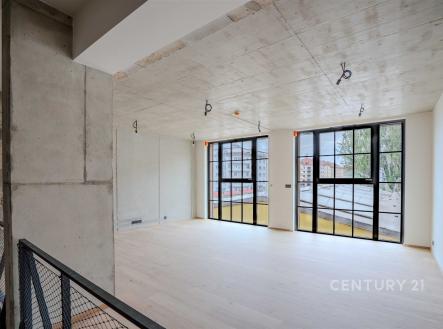 Světlý obývací pokoj s velkými okny, betonovým stropem a dřevěnou podlahou nabízí moderní a industriální atmosféru. | Prodej bytu, 4+kk, 176 m²
