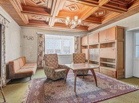 Obývací pokoj s dřevěným stropem, světlým kobercem a velkými okny, retro styl s nábytkem z 60. let, ideální pro renovaci. | Prodej - dům/vila, 187 m²