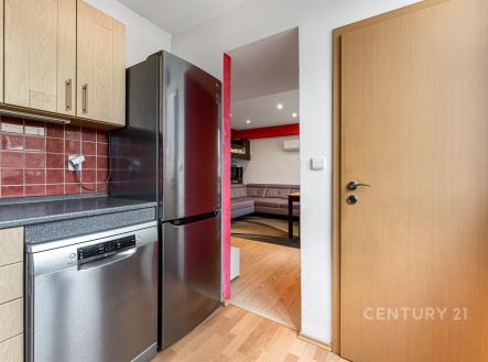 Kuchyň s moderními spotřebiči, dřevěnými skříňkami a parketovou podlahou, navazující na světlý obývací pokoj s velkými okny. | Prodej bytu, 2+1, 56 m²