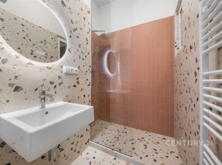 Moderní koupelna s terazzo obklady, prostorným sprchovým koutem a kulatým zrcadlem, elegantní a světlý design. | Pronájem bytu, 2+kk, 52 m²