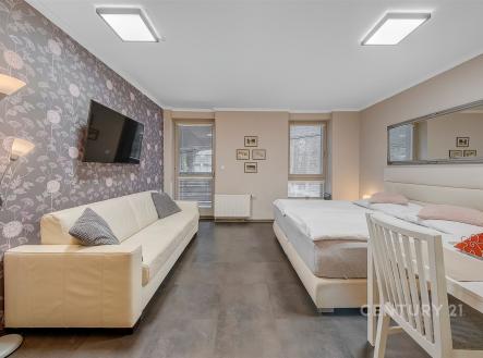 Prostorná ložnice s moderními prvky, parketová podlaha, velká okna, elegantní tapety na zdi, vybavená světlem a pohodlným nábytkem. | Prodej bytu, 1+kk, 32 m²