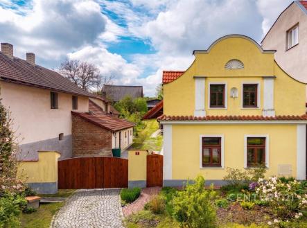 Tradiční fasáda rodinného domu s žlutou omítkou a dřevěnými okny, dlážděný chodník, udržovaná zahrada, historický styl. | Prodej - dům/vila, 245 m²