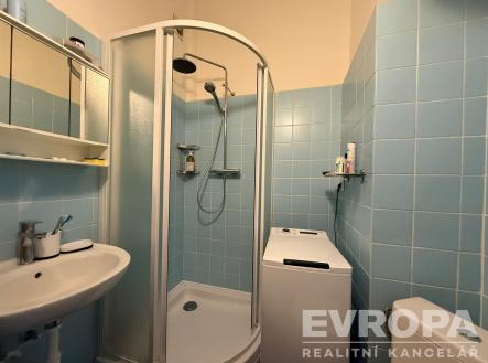 Koupelna s modrými dlaždicemi, sprchovým koutem a moderní sanitou, obsahuje také pračku a úložné police, vhodná pro rekonstrukci. | Pronájem bytu, 1+kk, 25 m²