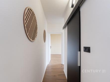 Úzká chodba s moderními prvky, dřevěná podlaha a posuvné dveře. Minimalistický design a dekorativní prvky na stěnách. | Prodej bytu, 2+1, 58 m²