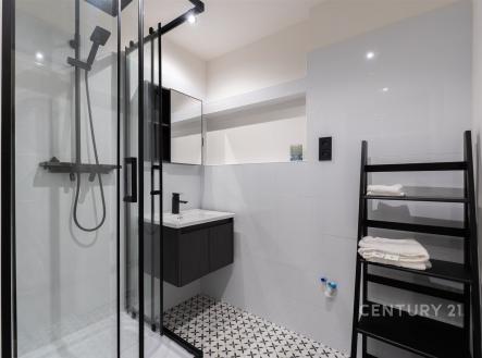 Moderní koupelna s proskleným sprchovým koutem, bílými dlaždicemi a dlažbou s geometrickým vzorem, elegantní černé prvky dodávají styl. | Prodej bytu, 2+1, 58 m²