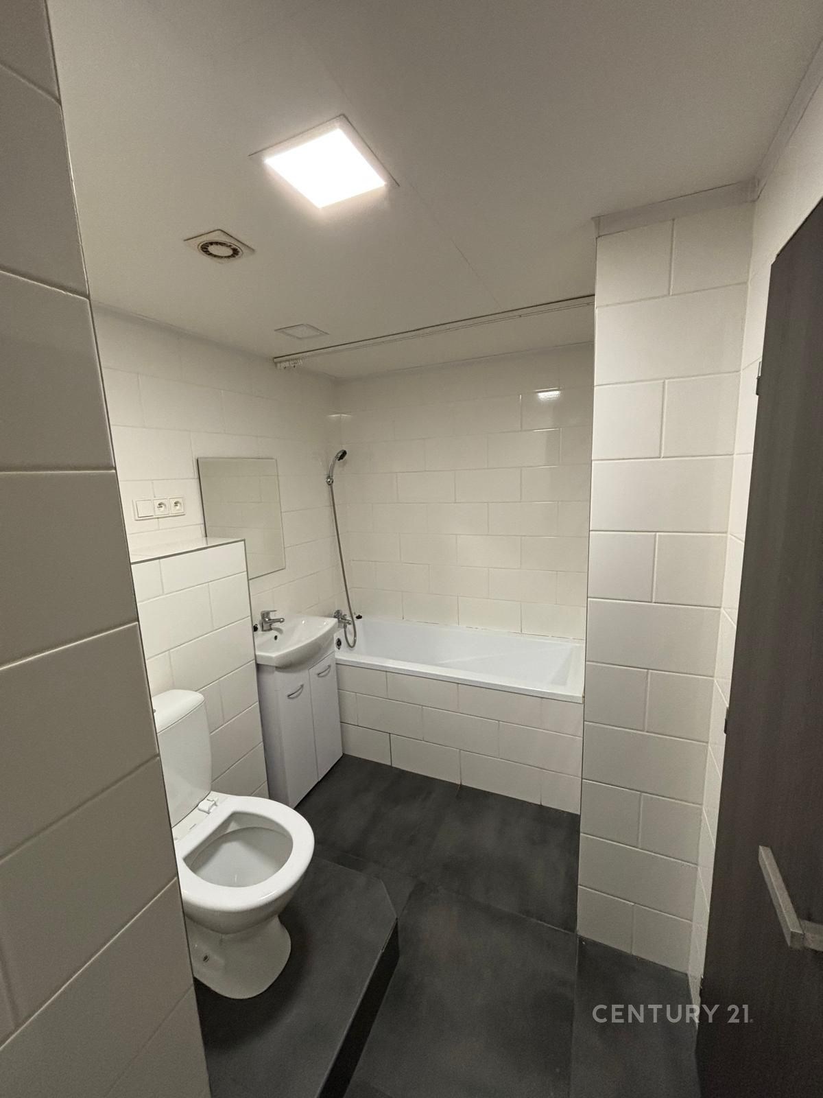 Koupelna s dlažbou, bílými obklady a vanou, vybavená moderním sanitárním zařízením, ideální pro rekonstruovaný byt.