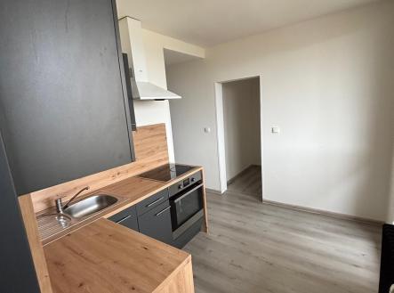 Kompaktní kuchyň s tmavou linkou, dřevěným obložením a moderními spotřebiči, světlá podlaha, minimalistický styl. | Pronájem bytu, 3+1, 69 m²