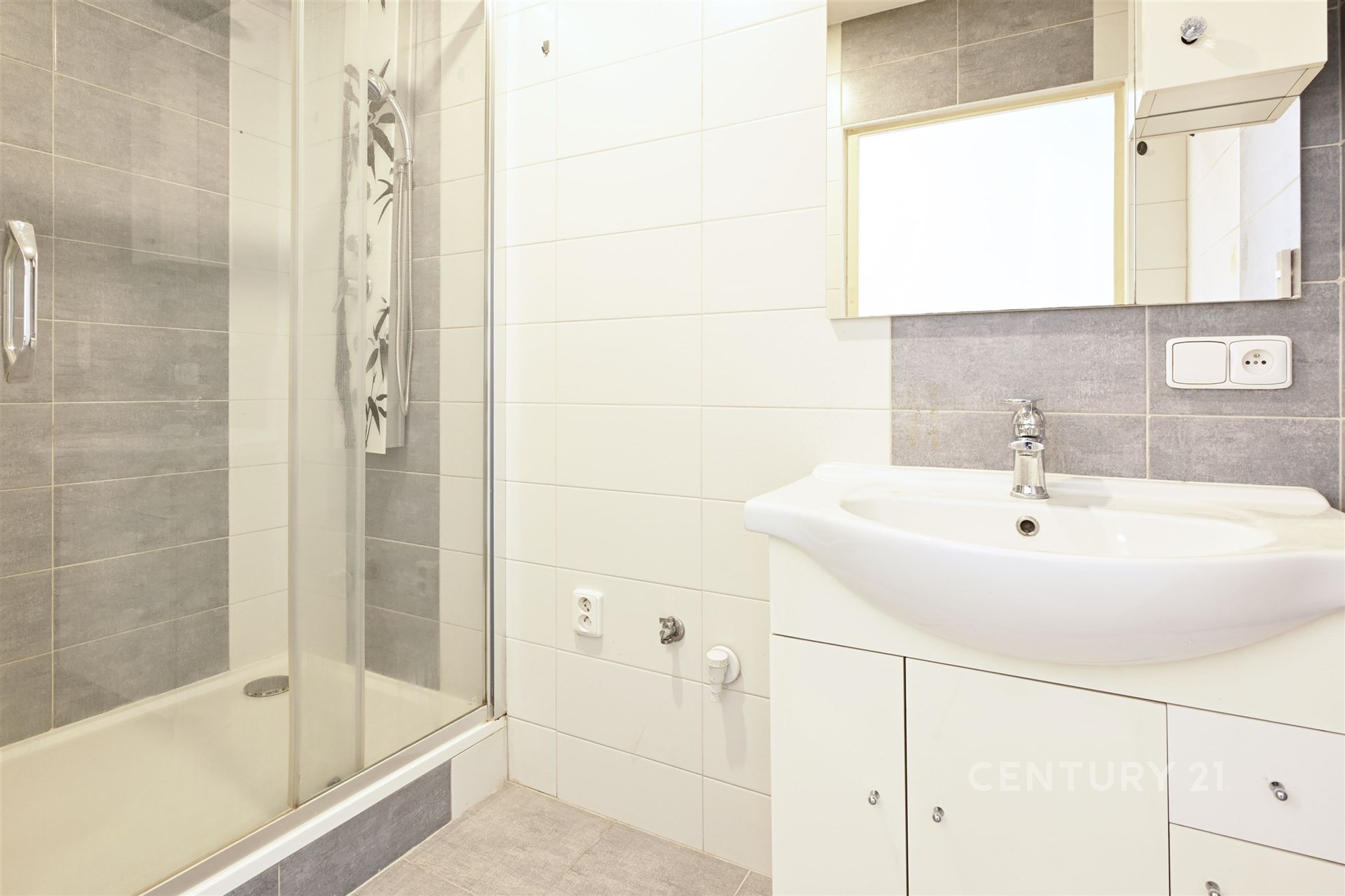 Moderní koupelna s betonovou dlažbou, sprchovým koutem a bílým umyvadlem. Kombinace šedých a bílých obkladů vytváří čistý vzhled.