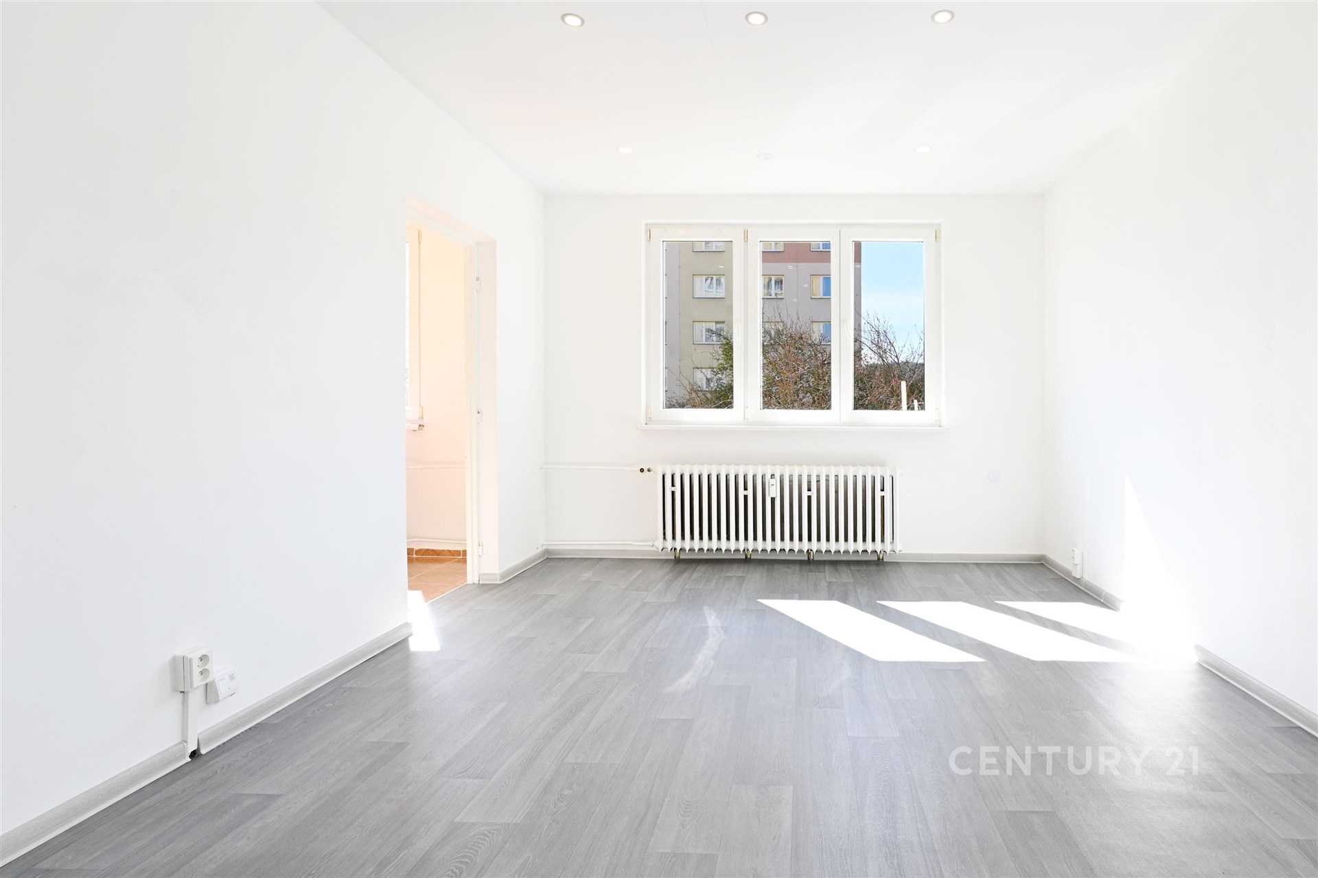 Světlý obývací pokoj s velkými okny, moderní parketová podlaha, bílý strop s vestavěným osvětlením, nově rekonstruovaný stav.