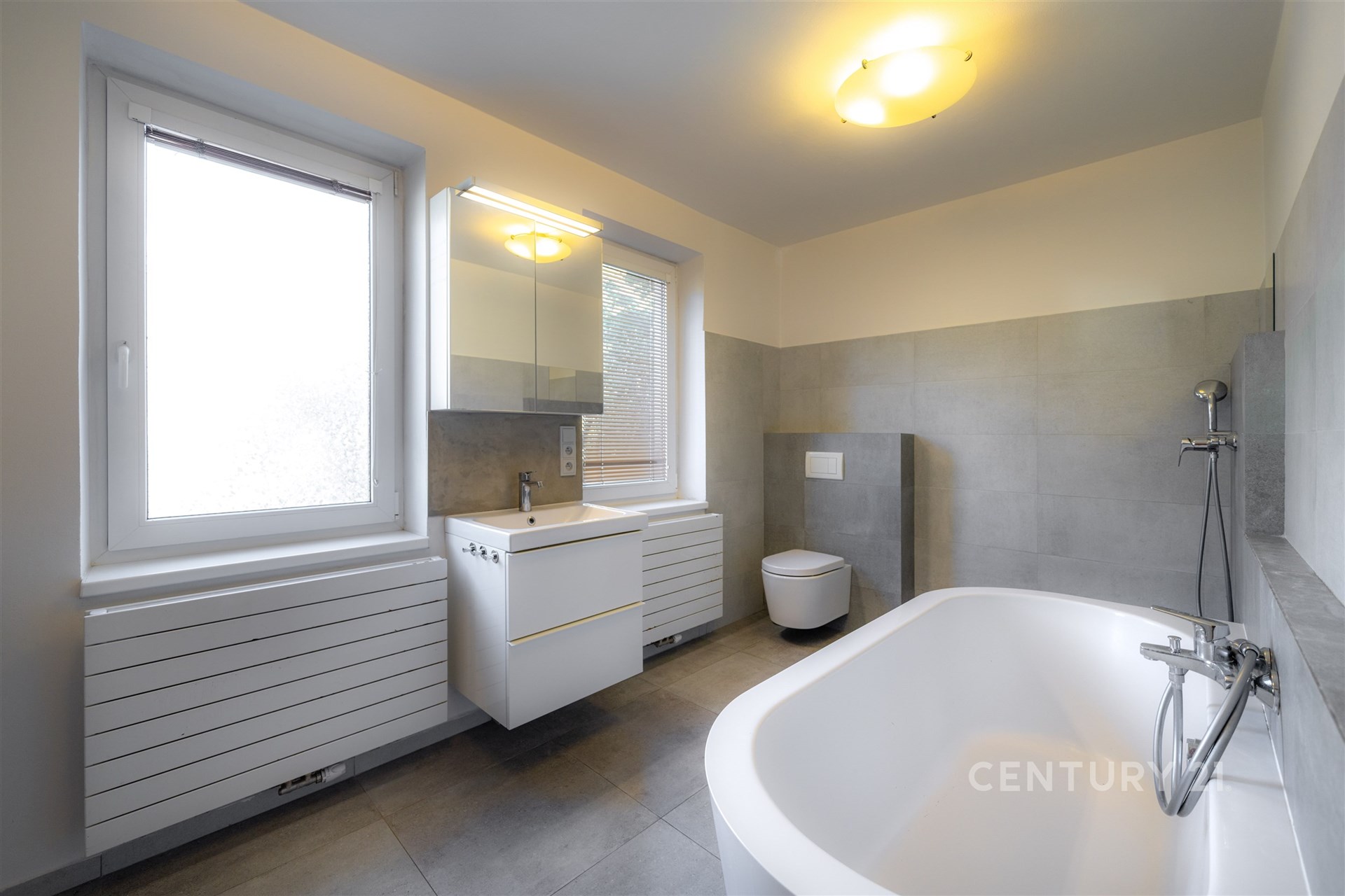 Prostorná koupelna s moderní dlažbou, velkými okny a novým osvětlením nabízí elegantní a světlý prostor k relaxaci.