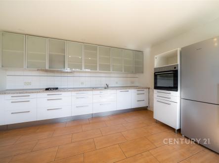 Prostorná a světlá kuchyň s moderními vestavěnými spotřebiči, dřevěnou podlahou a skříňkami s matnými skleněnými dvířky. | Prodej - dům/vila, 217 m²