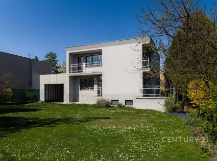 Moderní rodinný dům s bílou fasádou a velkými okny, nacházející se uprostřed prostorné zahrady s udržovaným trávníkem. | Prodej - dům/vila, 217 m²
