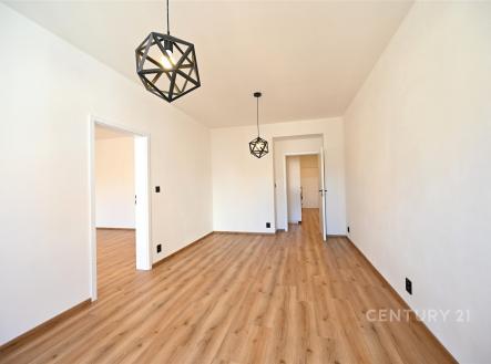 Světlý obývací pokoj s parketovou podlahou, moderním osvětlením a čistými bílými stěnami, vytváří elegantní a prostorný interiér. | Pronájem bytu, 2+kk, 86 m²