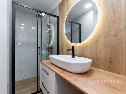 Moderní koupelna s velkým zrcadlem, dřevěným obkladem a sprchovým koutem. Stěny z kvalitní dlažby dodávají elegantní vzhled. | Prodej bytu, 2+kk, 35 m²