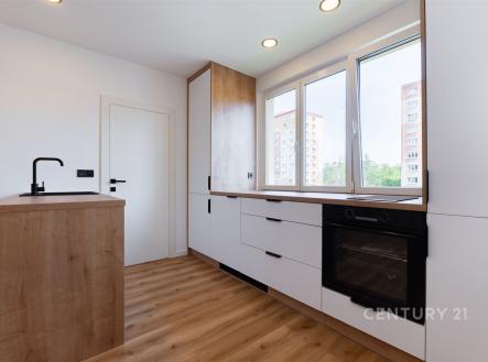 Moderní kuchyň s parketovou podlahou, vestavěnou troubou a velkými okny, nabízející světlý a vzdušný prostor. | Prodej bytu, 2+kk, 35 m²