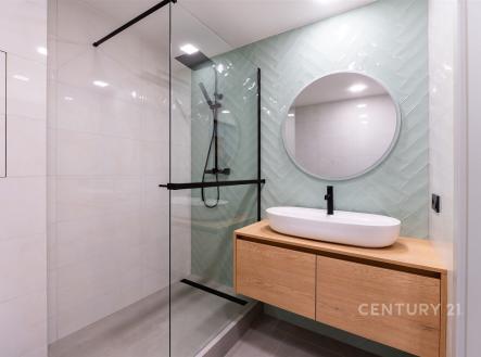 Moderní koupelna s proskleným sprchovým koutem, dřevěným umyvadlovým pultem a světlými obklady, které dodávají prostoru elegantní vzhled. | Prodej bytu, 3+kk, 54 m²