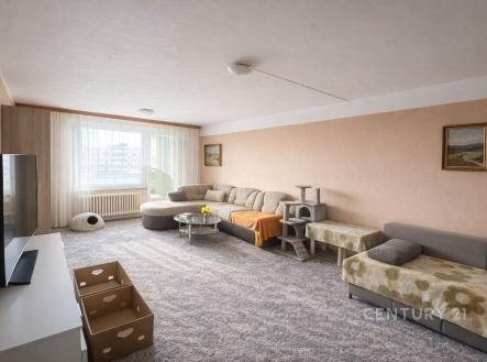 Prostorný obývací pokoj se světlým koberce, velkými okny a útulným nábytkem, nabízí světlý interiér s moderním designem. | Prodej bytu, 1+1, 45 m²