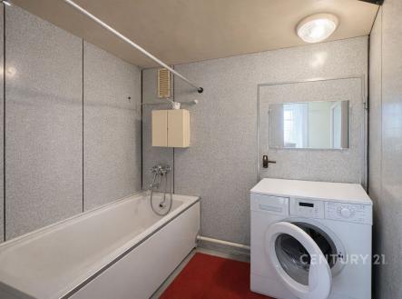 Koupelna s vanou, pračkou a vestavěnou skříňkou, s moderními panelovými stěnami a stropním osvětlením, nabízí praktický prostor v bytě. | Prodej bytu, 1+1, 45 m²