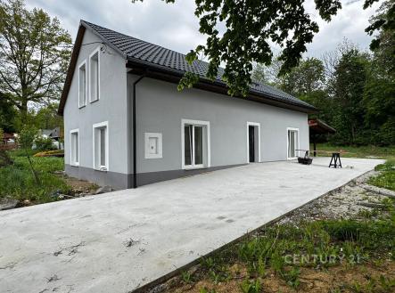 Moderní rodinný dům s šedou fasádou a tmavou střechou, obklopený zelení. Venkovní prostor zahrnuje betonovou terasu, ideální pro relaxaci. | Prodej - dům/vila, 190 m²