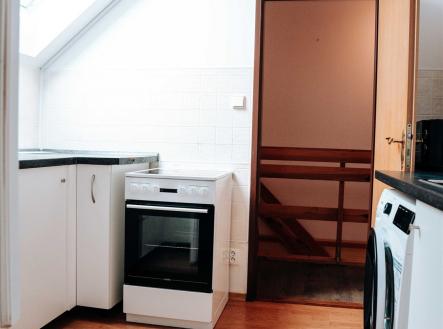 Kuchyň v podkroví, světlá dřevěná podlaha, střešní okno, moderní spotřebiče, bílá kuchyňská linka. | Pronájem bytu, 3+1, 83 m²