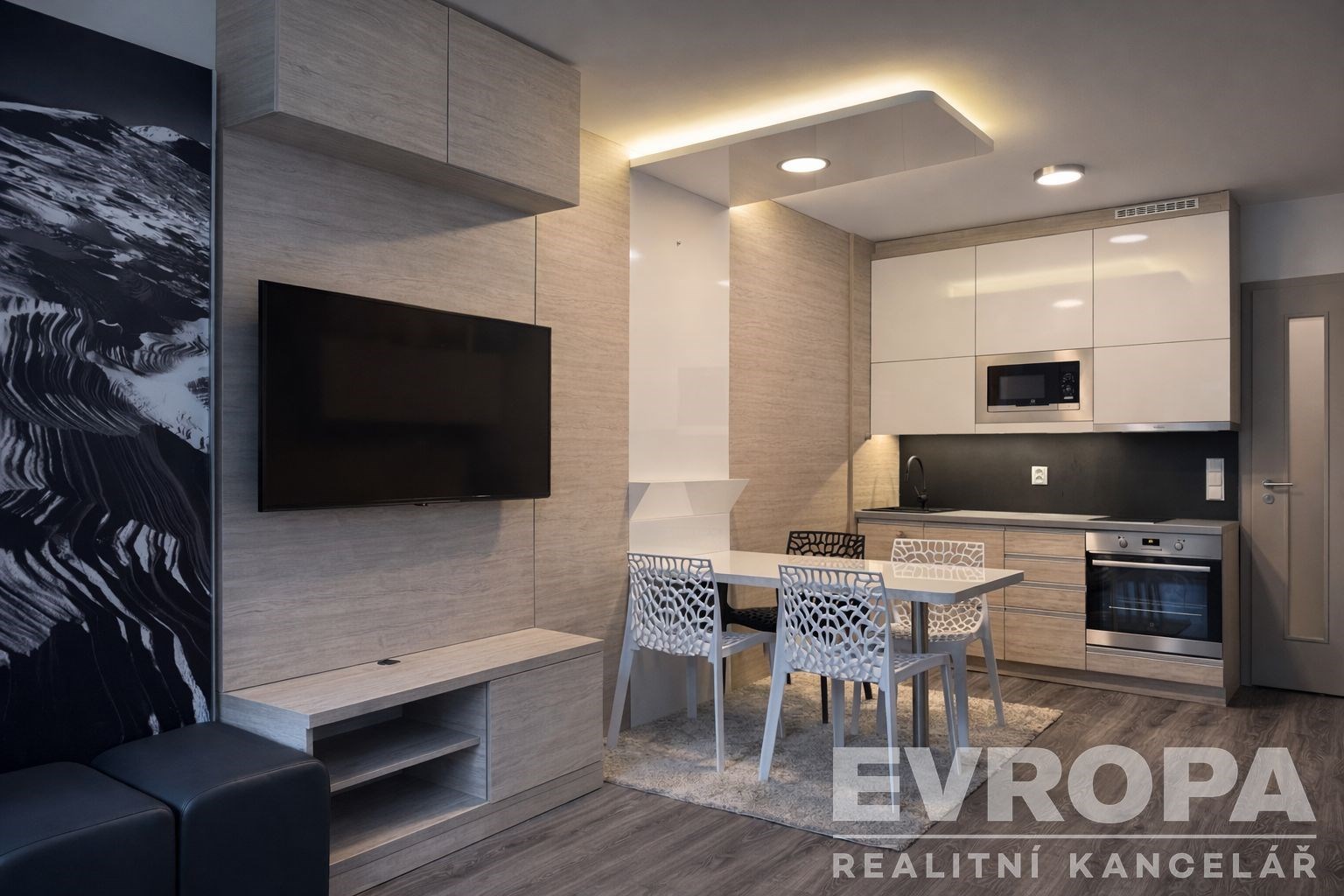 Moderní kuchyň s vestavěnými spotřebiči, světlým dřevěným obkladem a laminátovou podlahou, spojená s jídelním koutem s moderními židlemi.