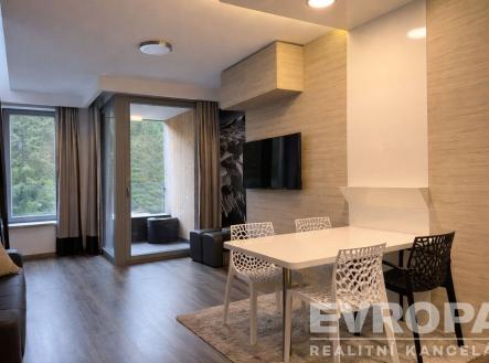 Moderní obývací pokoj s dřevěnou podlahou, velkými okny a elegantním nábytkem. | Prodej bytu, 2+kk, 56 m²