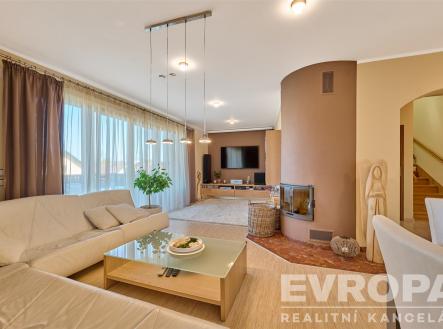 Prostorný obývací pokoj s krbem, parketovou podlahou a velkými okny nabízí moderní a světlý interiér. | Prodej - dům/vila, 229 m²