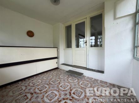 Uzavřená veranda s dlažbou a velkými okny, dřevěné dveře vedoucí do další místnosti, světlý prostor ideální pro relaxaci. | Pronájem bytu, 1+kk, 27 m²