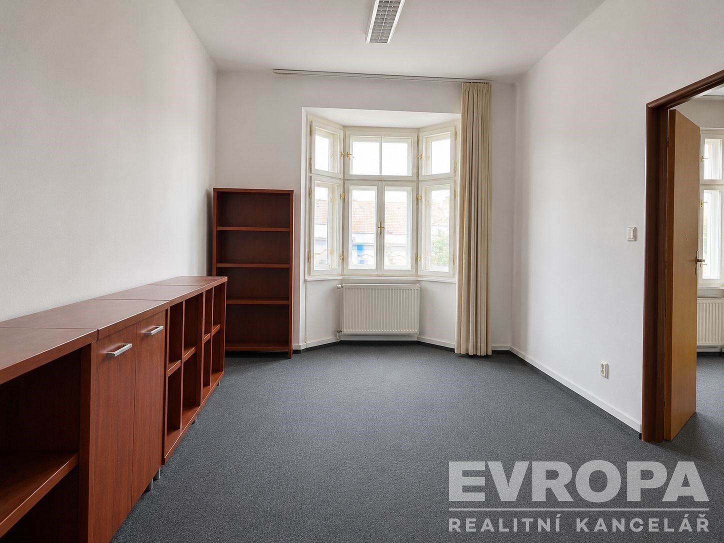 Pracovna s kobercem, vestavěnými skříněmi a velkými okny, které poskytují dostatek světla, ideální pro moderní kancelářské prostředí.