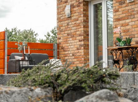 Terasa s cihlovou zídkou a moderním nábytkem, vhodná k venkovnímu posezení, doplněná o dekorativní dřevěné prvky a rostliny na stolku. | Prodej - dům/vila, 203 m²