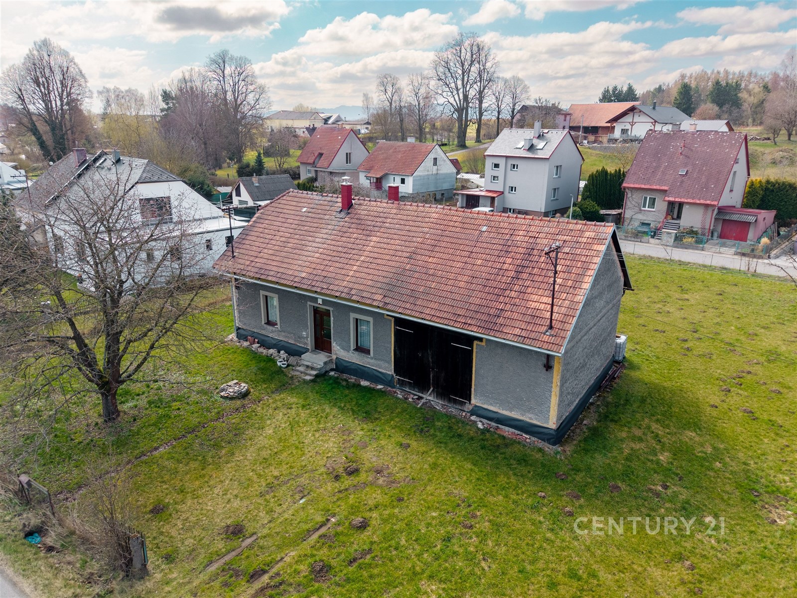 Samostatně stojící dům s červenou střechou na prostorném pozemku, zasazený do klidné vesnické oblasti, ideální pro rekonstrukci.