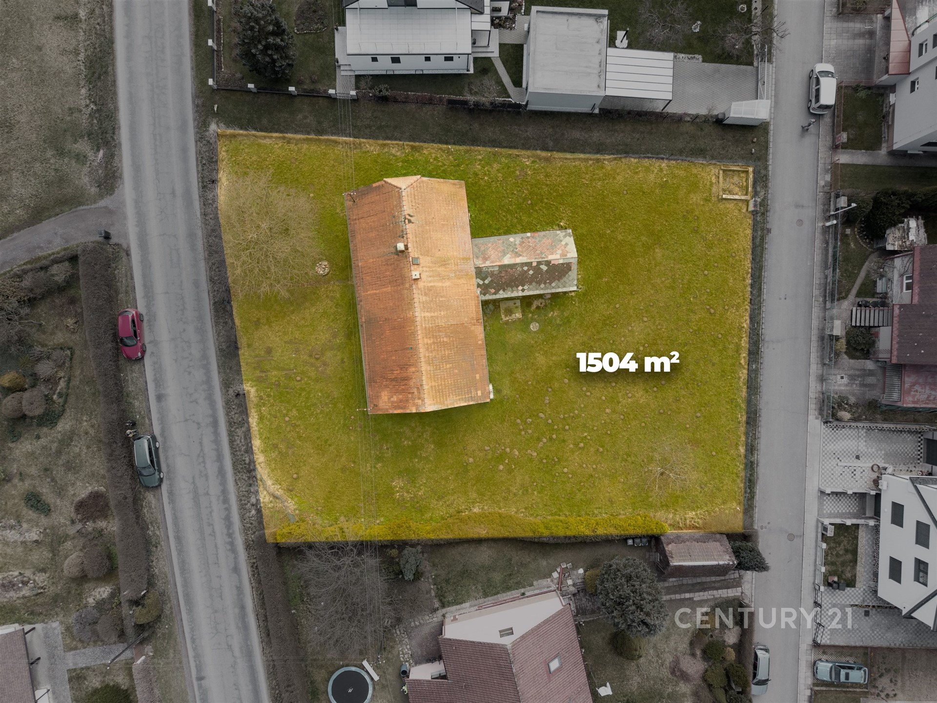 Letecký pohled na pozemek se starším domem s červenou střechou, rozloha 1504 m², klidná lokalita, ideální pro novou výstavbu nebo rekonstrukci.