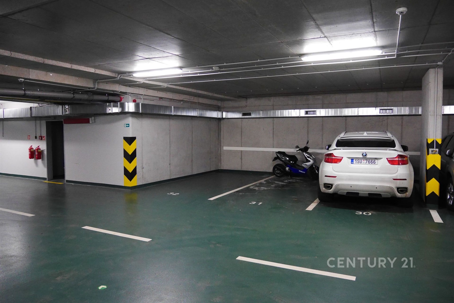 "Podzemní garáž s moderní povrchovou úpravou, dobře osvětlený prostor a vysoké stropy, ideální pro bezpečné parkování vozidel"