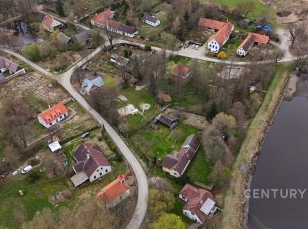 Letecký pohled na malebnou vesnici s tradičními domy, červenými střechami a přilehlým rybníkem, zasazenou do klidné krajiny. | Prodej - pozemek, ostatní, 3 617 m²