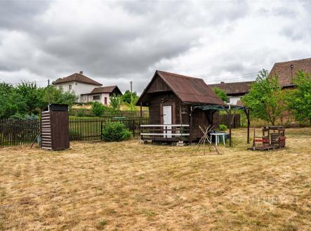 Zahrada s dřevěnými zahradními domky, obklopená plotem, s několika mladými stromy a suchým travnatým povrchem, vhodná pro rekreační účely. | Prodej - pozemek pro bydlení, 1 139 m²