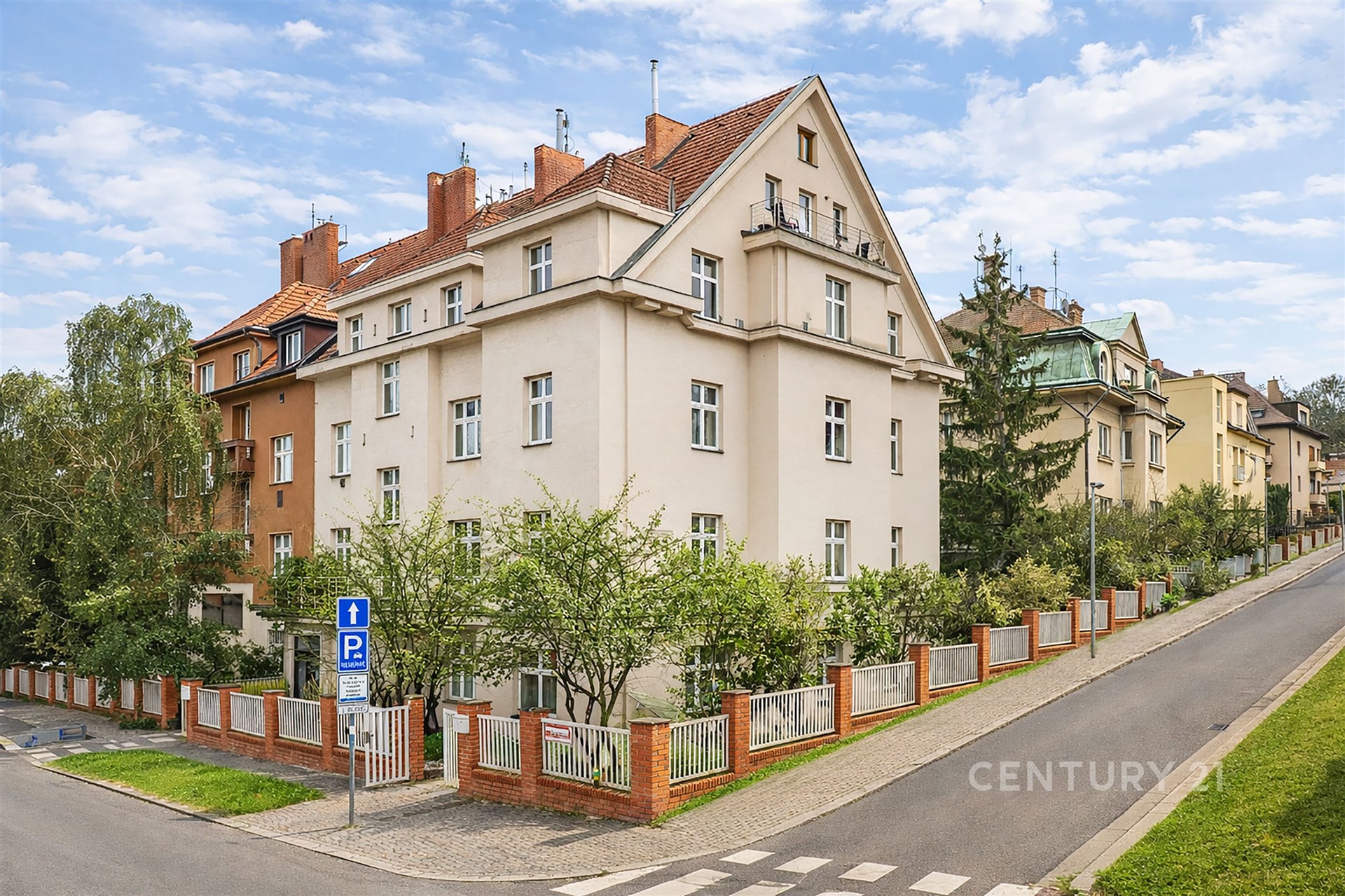 Vícepatrový dům s červenou střechou a zahradou, který se nachází ve vilové čtvrti, ukazuje udržovaný exteriér a klidné okolí.