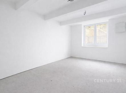 Rekonstruovaný světlý pokoj s bílými stěnami, betonovou podlahou a velkým oknem poskytujícím přirozené světlo. | Prodej bytu, 2+kk, 47 m²