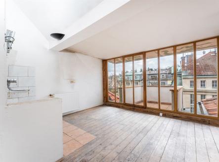 Podkrovní místnost s dřevěnými podlahami a velkými okny, nabízející výhled na historické budovy, ideální pro moderní rekonstrukci. | Prodej bytu, 2+kk, 54 m²