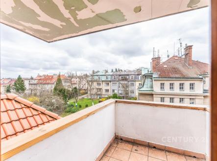 Výhled z balkónu s dlažbou a rustikálním zábradlím, nabízející pohled na klidnou rezidenční čtvrť s upravenými střechami a zahradami. | Prodej bytu, 2+kk, 54 m²