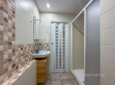 Koupelna s moderní dlažbou, sprchovým koutem a dřevěnou skříňkou, světlé dlaždice vytvářejí čistý a prostorný vzhled. | Pronájem bytu, 1+kk, 27 m²