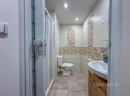Moderní koupelna s dlažbou, sprchovým koutem a dřevěnou skříňkou pod umyvadlem, nabízí světlý interiér a kvalitní vybavení. | Pronájem bytu, 1+kk, 27 m²