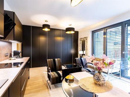 Moderní obývací pokoj s parketovou podlahou, velkými okny a elegantním černým nábytkem, ideální pro světlé a stylové bydlení. | Pronájem bytu, 1+kk, 37 m²